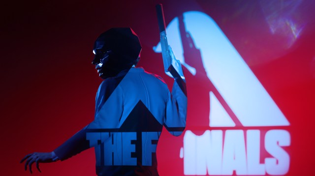 A masked player posing with a silenced pistol in front of the THE FINALS logo.
